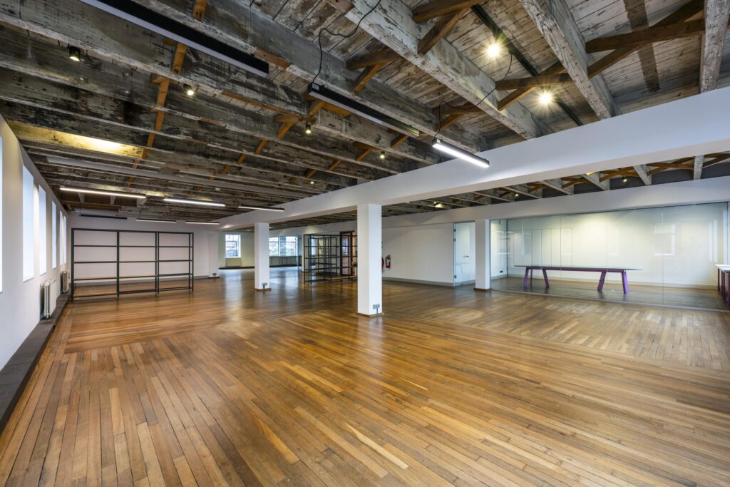 Ruim en licht industrieel kantoorinterieur aan de De Ruijterkade met houten vloer, glazen vergaderruimte en zichtbare houten plafondbalken.